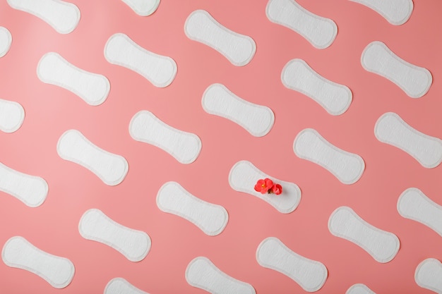 Sanitary pads on a pink background in the form of a diagonal pattern of repetitions, with a red flower on the pad.