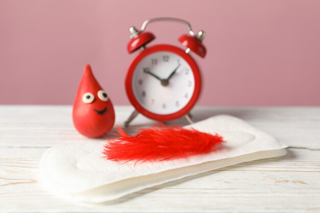 Sanitary pads with feather, decorative blood drop and alarm clock on wooden table