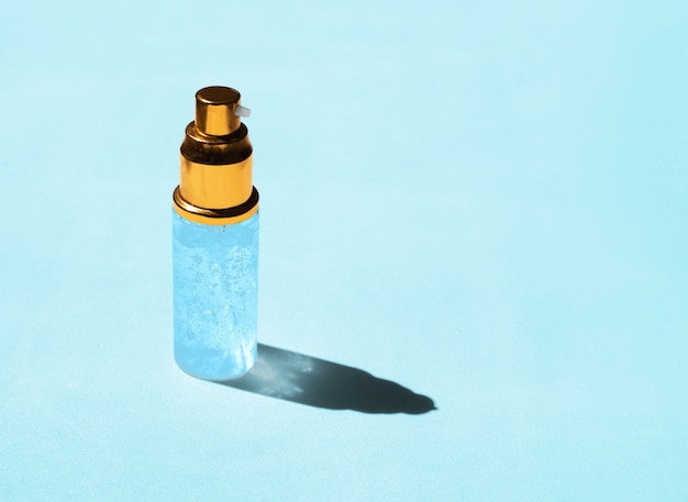 Gel igienizzante trasparente su sfondo blu con un'ombra traslucida del sole splendente