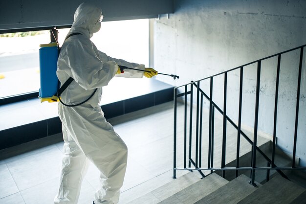 Sanitizing worker cleaning up the staircase at the shopping mall with an antiseptic to prevent covid-19 spread. A man in a disinfection suit sprays stairs. Healthcare, quarantine and hygiene concept.