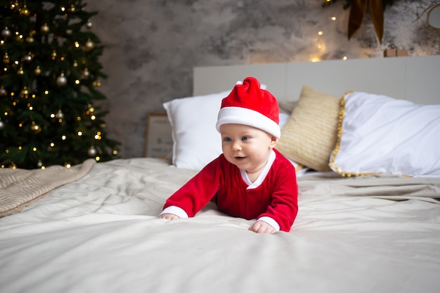 サンタの赤ちゃん。赤いクリスマスキャップを着て、ベッドの上のかわいい子