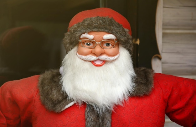 Большая пластиковая фигура Санта-Клауса с классической одеждой Санта-Клауса рядом с деревянным домом