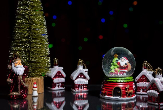 Photo santa claus christmas tree and a snow globe on a dark glossy table among toy houses