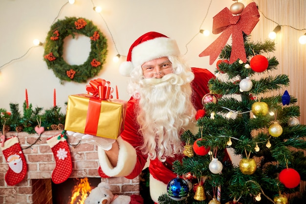 Babbo natale all'albero di natale con un regalo in mano sorridente a natale, capodanno.