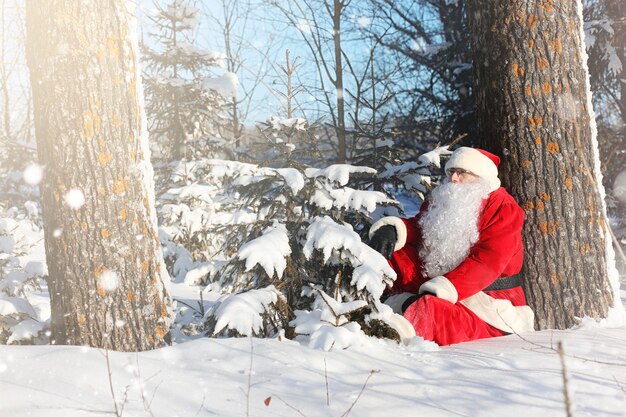 Santa Claus comes with gifts from the outdoor. Santa in a red suit with a beard and wearing glasses is walking along the road to Christmas. Father Christmas brings gifts to children.