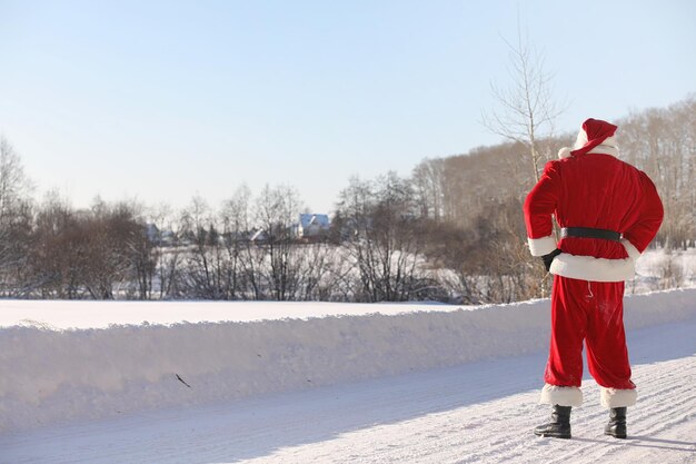 Santa Claus comes with gifts from the outside. Santa in red suit with a beard and wearing glasses is walking along the road to Christmas. Father Christmas brings gifts to children.