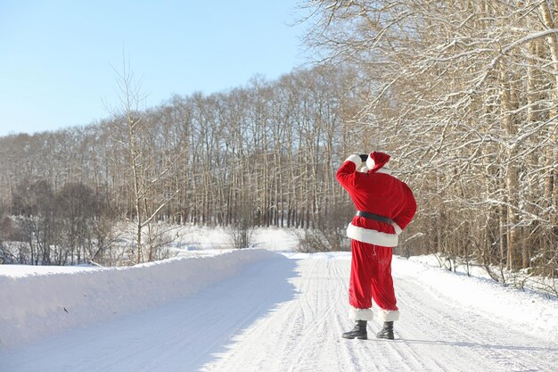 Santa claus comes with gifts from the outside santa in a red suit with a beard and wearing glasses is walking along the road to christmas father christmas brings gifts to children