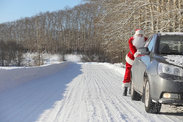 Santa Claus comes with gifts from the outside. Santa in red suit with a beard and wearing glasses is walking along the road to Christmas. Father Christmas brings gifts to children.