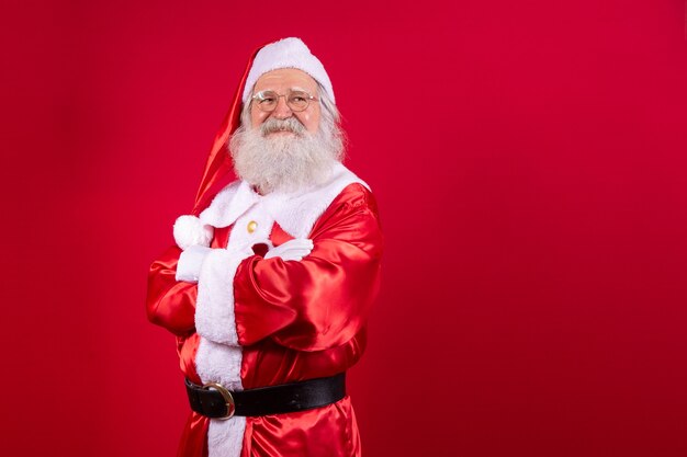 Santa Claus crossed arms on red background. Kind bearded Santa Claus with arms folded over red background. Studio shot of realistic Santa Claus.