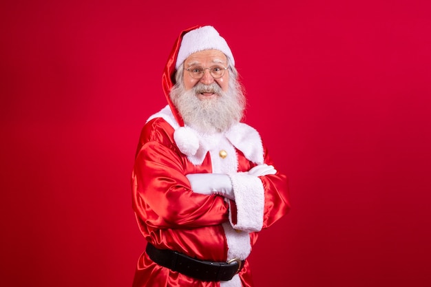 산타 클로스는 빨간색 배경에 팔짱을 끼고 있습니다. 빨간 배경 위에 팔짱을 끼고 수염난 산타클로스 종류. 현실적인 산타 클로스의 스튜디오 샷입니다.