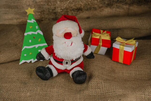 Foto bambola di babbo natale su tela su uno sfondo di albero di natale e due scatole regalo