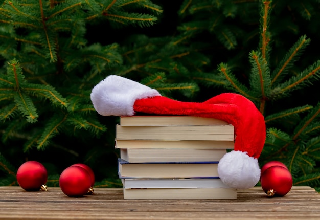 Santa Claus hat and books on wooden table with spruce branches on background