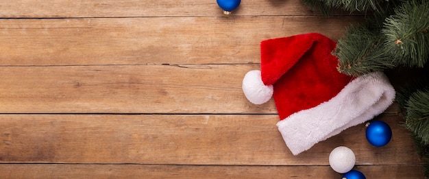 Santa Claus hat, gifts and branches of a Christmas tree on a wooden background. Top view, flat lay. Banner.