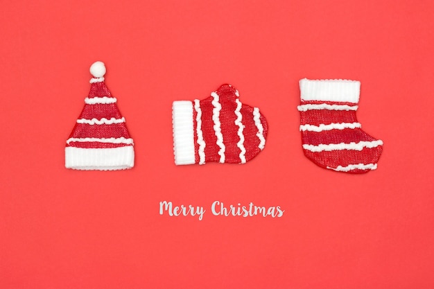 Santa Claus hat, glove, sock flat lay on red background with word merry christmas. Minimal style. Holiday concept.