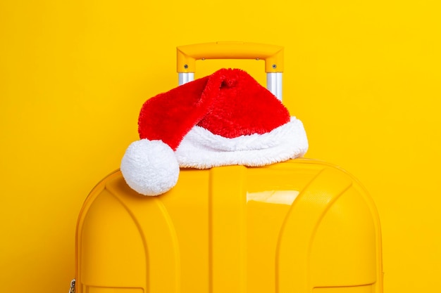 Santa Claus hat lies on top of a yellow suitcase on a yellow background