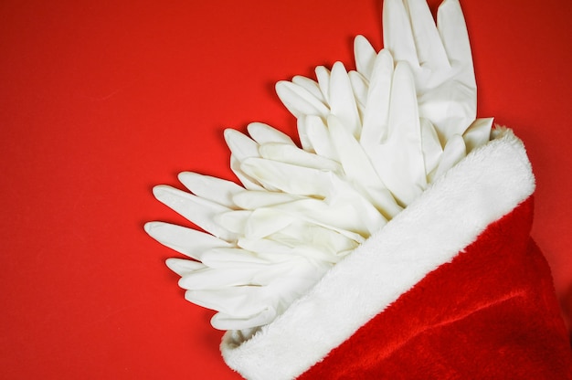 Шляпа Санта-Клауса с медицинскими перчатками на красном фоне