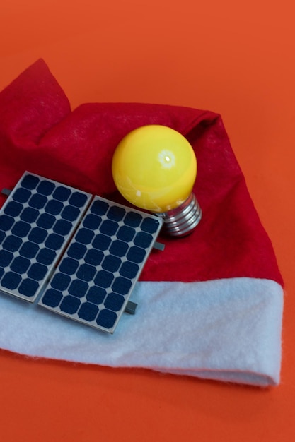 Photo santa claus hat with photovoltaic solar panel and lamp isolated on orange background. concept image.