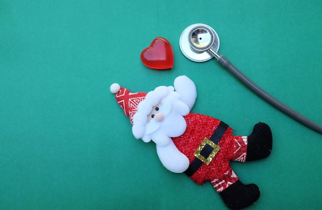 Photo santa claus and heart shape decoration by stethoscope on green table