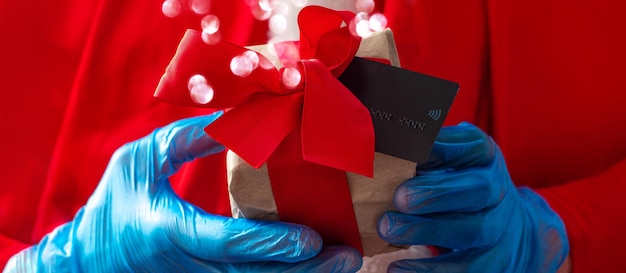 Santa Claus hold offers a gift box ribbon bow with credit card in hands in protective glovesChristmas New Year shopping