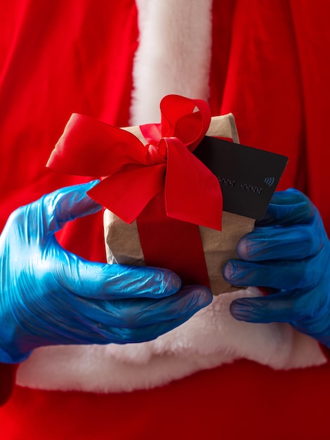 Santa Claus hold offers a gift box ribbon bow with credit card in hands in protective glovesChristmas New Year shopping