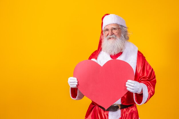 Santa Claus holding big red heart card in yellow background. Romantic Santa Claus.