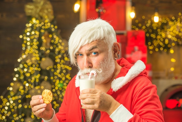 Santa Claus holding Christmas cookies and milk against Christmas tree background Milk and gingerbrea