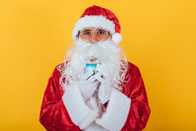 Santa claus holding a christmas snow globe, on yellow