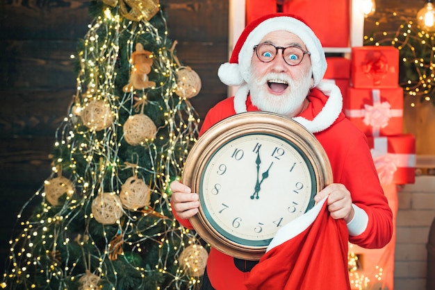 Santa Claus holding clock with countdown to Christmas or New Year Santa Claus in wooden home interio