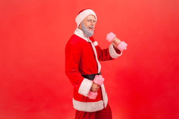 Санта-клаус держит гантели, тренирует руки, с азартом смотрит в камеру.