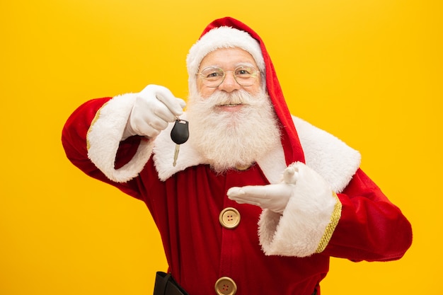 Санта-Клаус держит ключи автомобиля на желтом фоне.
