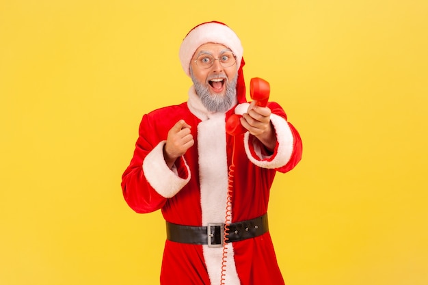 Babbo natale che tiene la cornetta del telefono fisso, chiamandoti per congratularsi con i fests