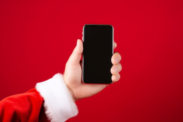 Санта-Клаус с мобильным телефоном, готовым к Рождеству на красном фоне студии