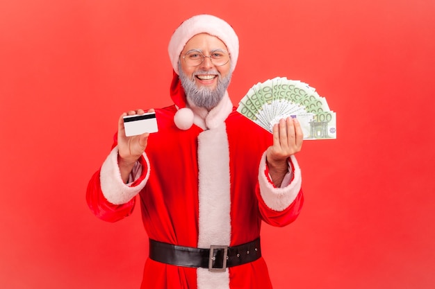 Santa claus holding showing fan of euro banknotes and credit card in hands.