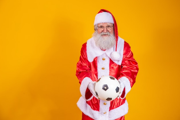 Santa Claus holding a soccer ball on yellow background.