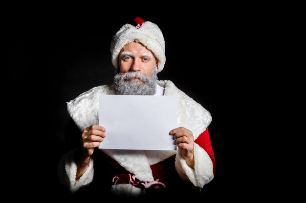 Santa claus houdt een blanco vel in zijn handen op een zwarte achtergrond