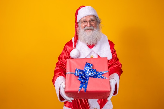 Santa claus houdt een geschenkdoos op gele achtergrond. kerstmis en nieuwjaar concept