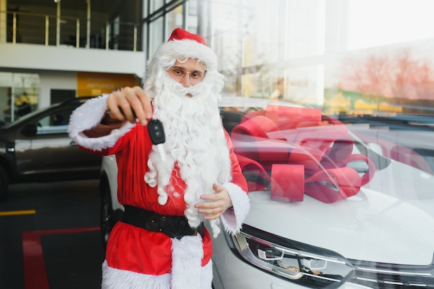 Santa Claus in de buurt van een nieuwe auto in een autodealer.