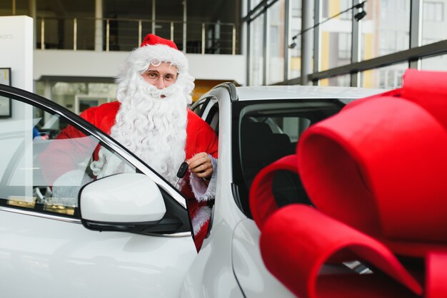 Santa Claus in de buurt van een nieuwe auto in een autodealer.