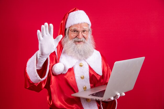 Santa Claus met behulp van een laptop op rode achtergrond.