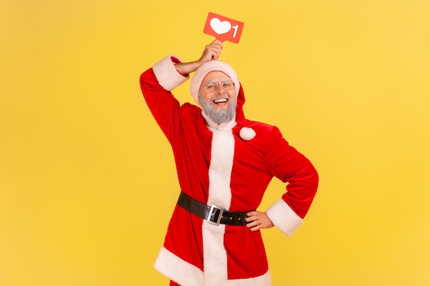 Santa claus met sociaal netwerk Heart Like-pictogram boven het hoofd, kijkend naar de camera met een brede glimlach.