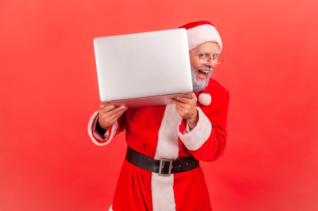 Santa claus posing peeking from laptop computer, laughing happily, winter holidays.