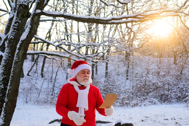 サンタクロースはウィッシュリストを読んで、雪に覆われたクリスマスの森を歩きます