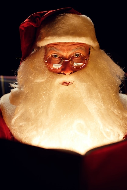 Babbo natale che legge un libro magico mentre era seduto in una stanza buia