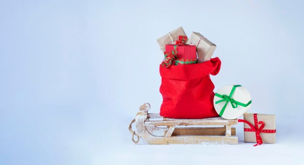 白い背景の上の木製のそりにクリスマスプレゼントとサンタクロース赤いバッグストックイメージ