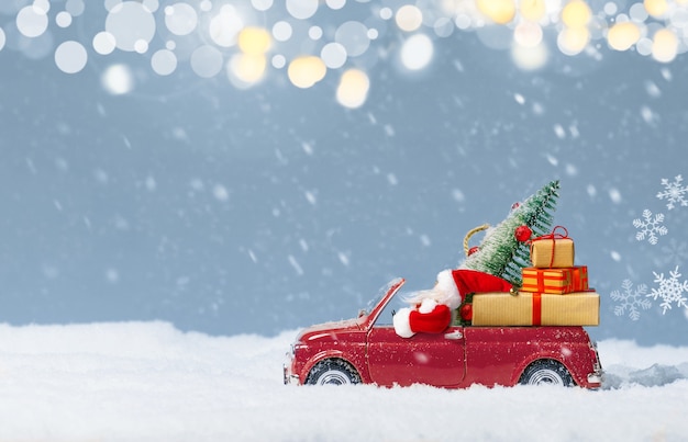 Santa Claus in Red car delivering christmas tree and presents at snowy background. Christmas or new year background. Holidays card. Copy space.