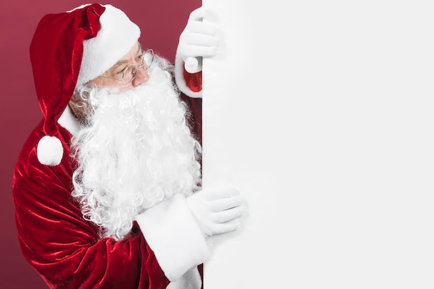 Foto babbo natale in cappello rosso guardando fuori dal muro bianco