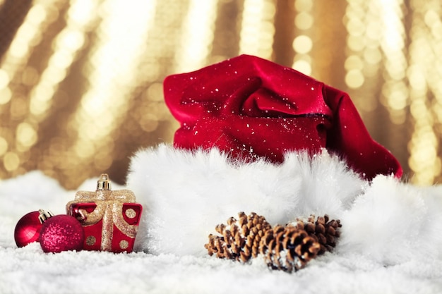 Santa Claus red hat with Christmas decorations on the artificial snow against golden background, close up