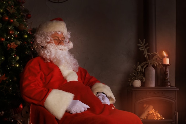 Santa Claus rust in een comfortabele stoel bij de open haard thuis.