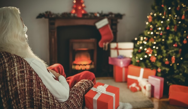 크리스마스 트리 근처 안락의자에 앉아 집에 선물을 들고 있는 산타클로스