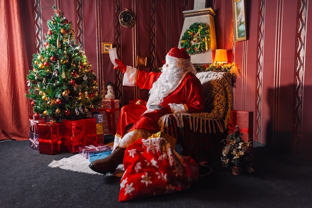 산타 클로스는 크리스마스 트리 옆에 앉아